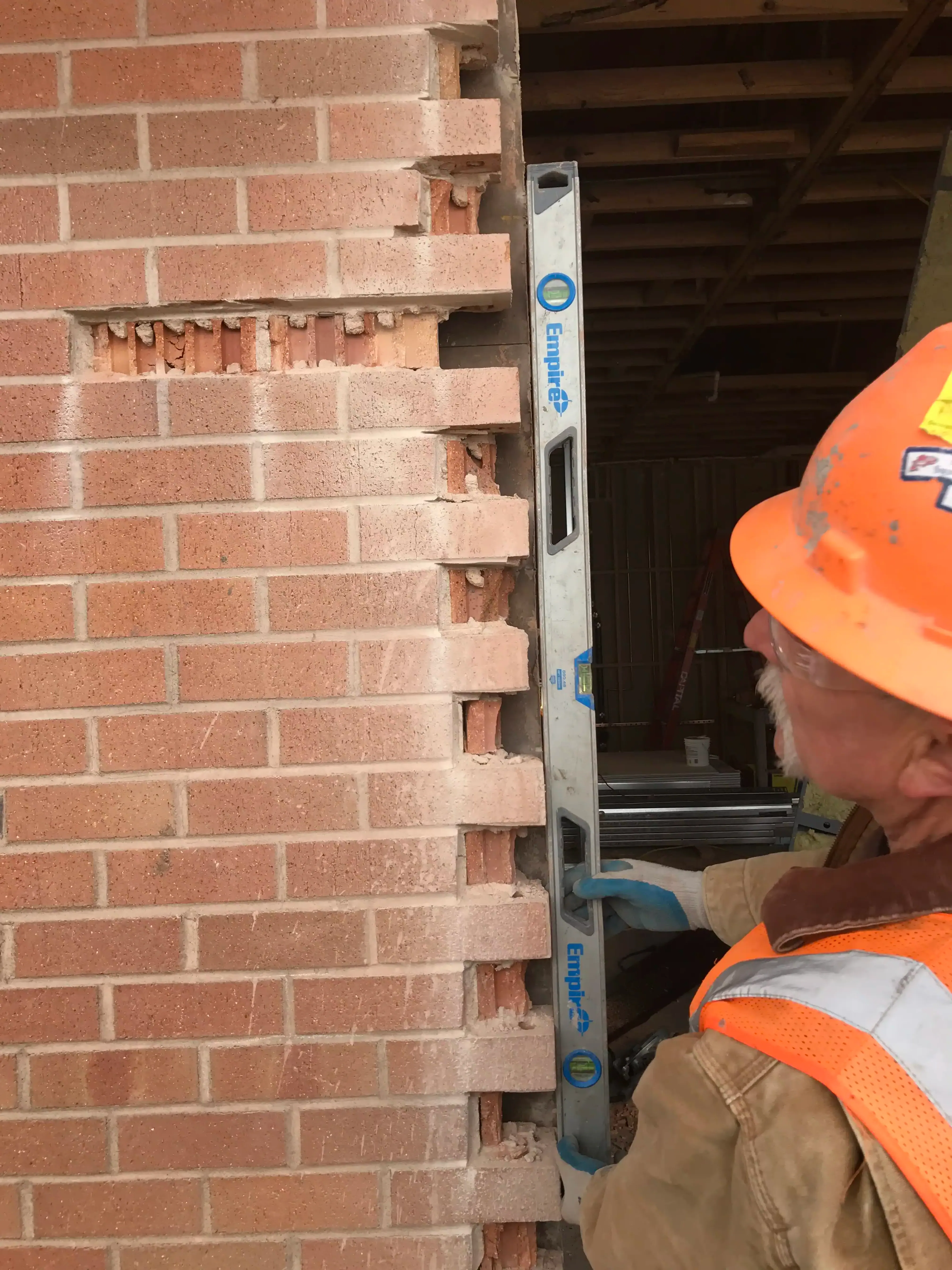 Photo showing a bubble level held up to the edge of brick veneer in which the original masonry is not plumb.