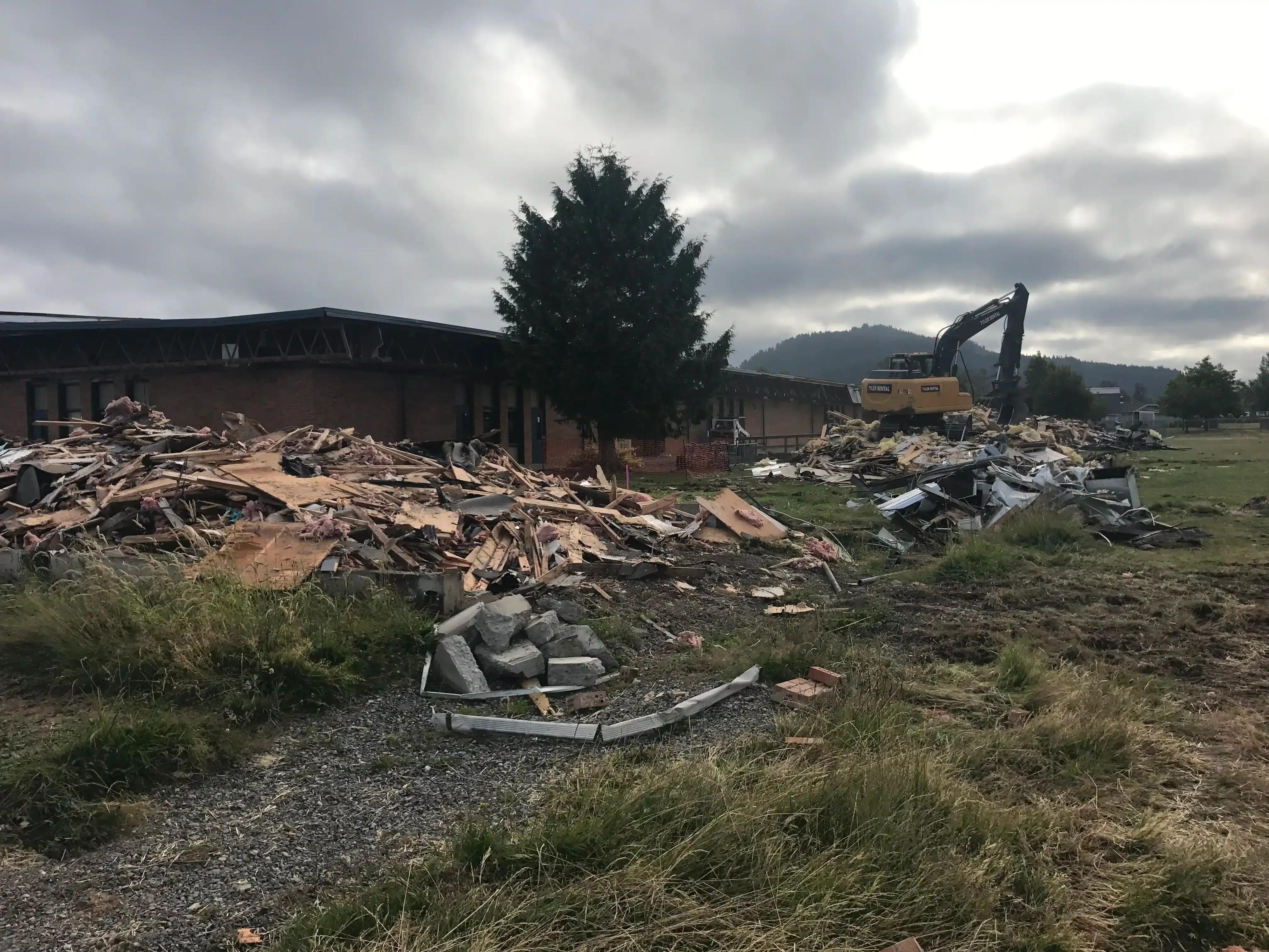 Photo of piles of demolition rubble with an excavator on top of one of the mounds.