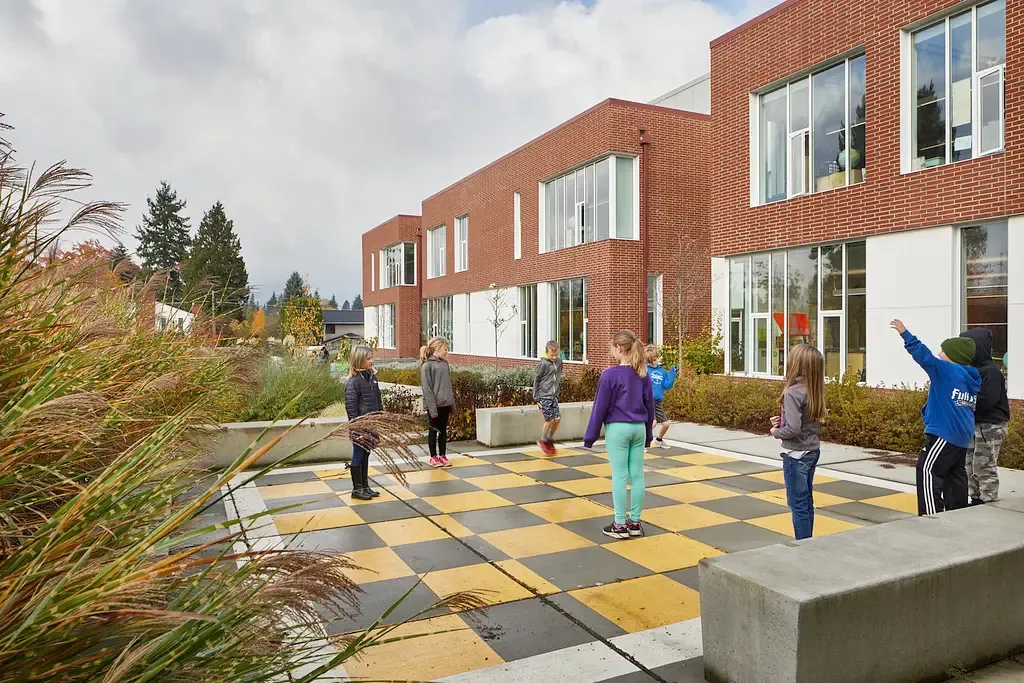 Photo taken outside the commons area featuring an outdoor checkers-board style concrete patio with children playing on it.